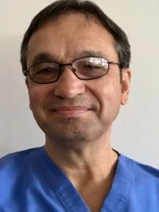 Dr. Onea in blue surgical scrubs and glasses smiling against plain white background